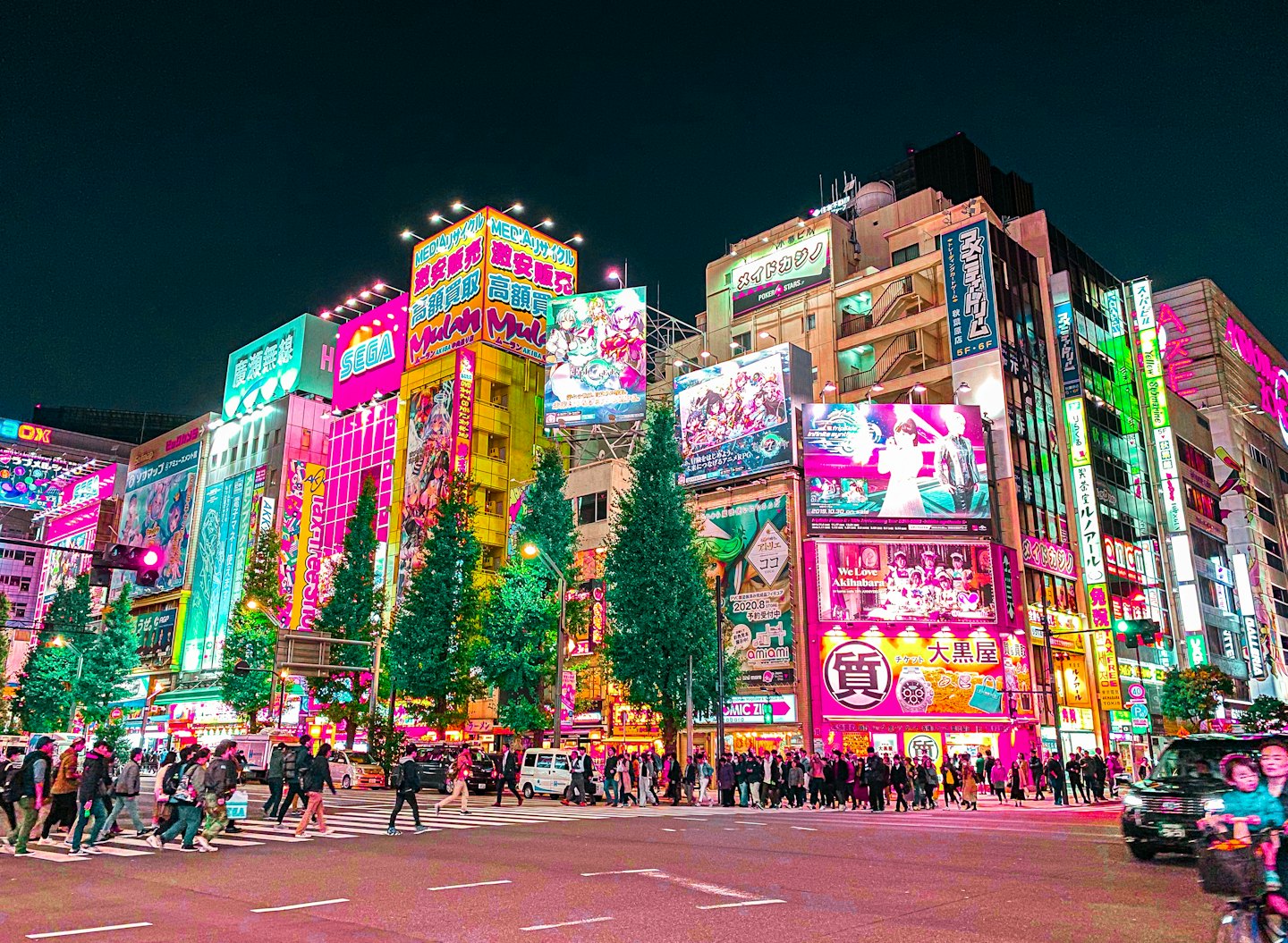 Nighttime Tokyo street crossing with neon signs and traffic.