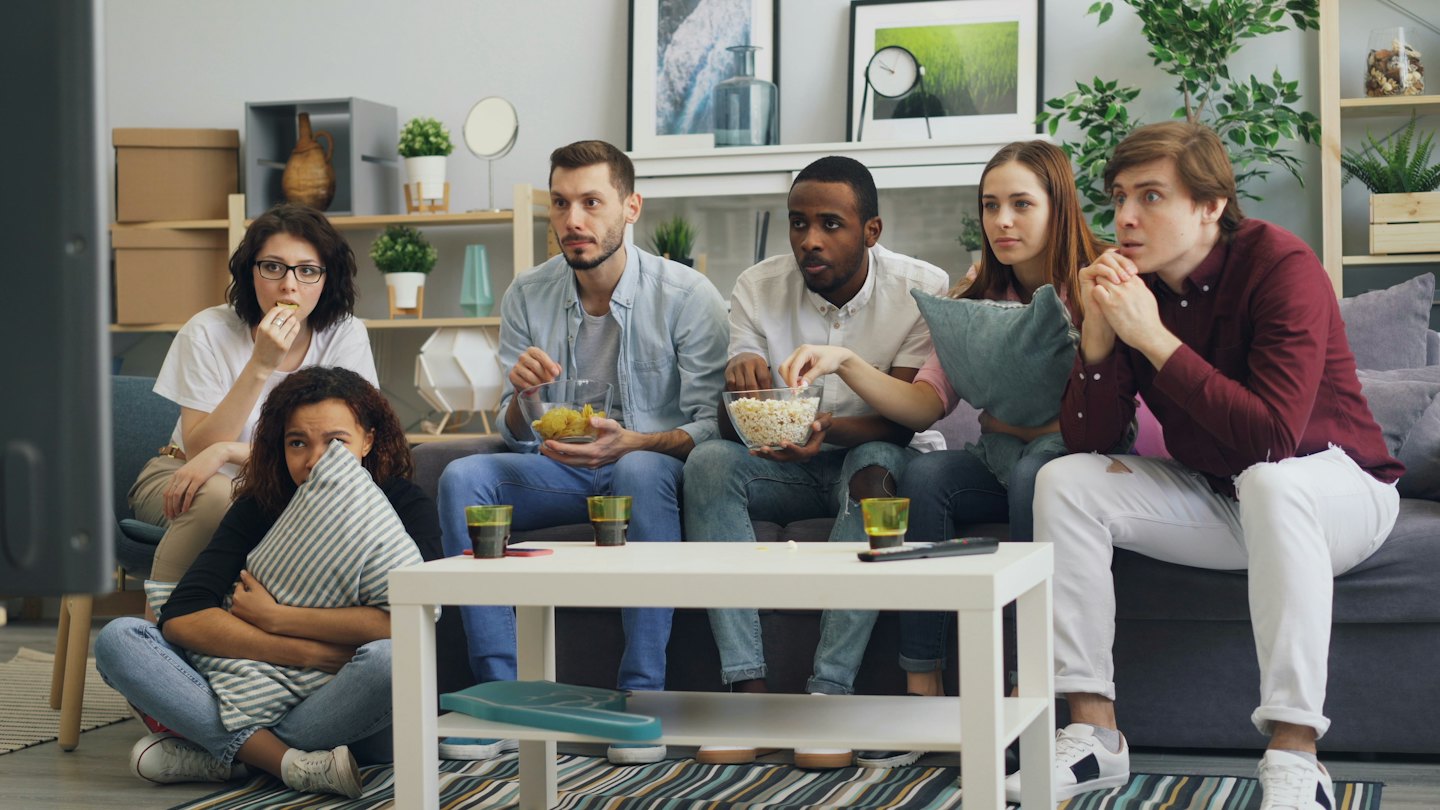 Young adults watch TV together in a living room.